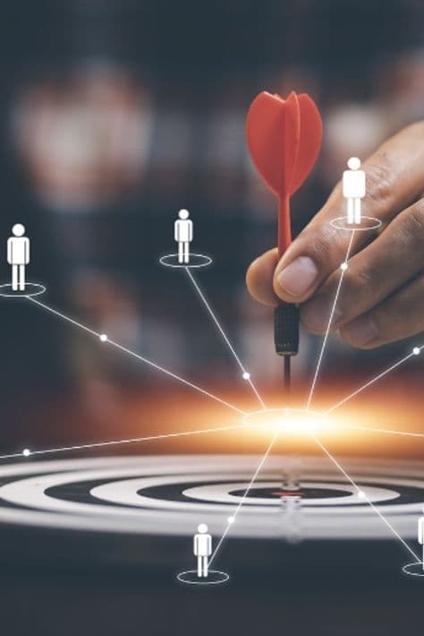 A hand placing a dart in a target at the centre of a network of figures
