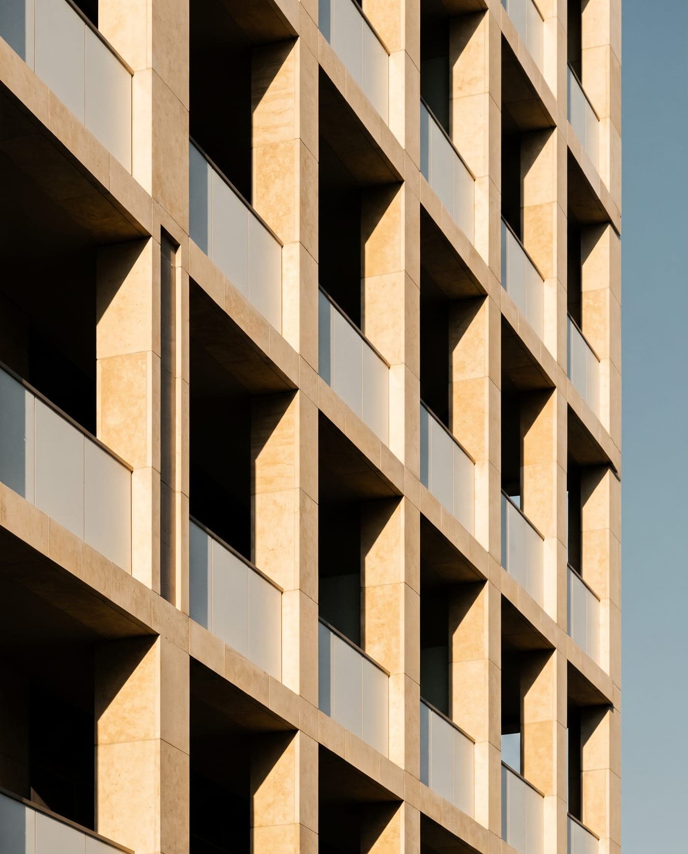 Repeating balconies and stone fins on a contemporary Dubai residential facade, catching low afternoon light.