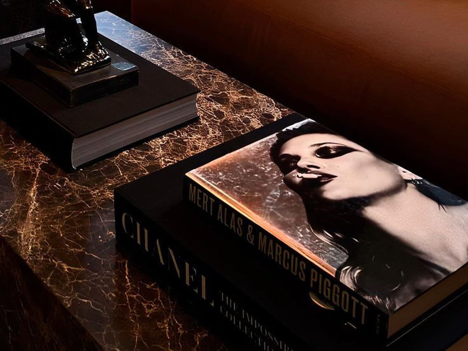 A small bronze figurine and a stack of designer coffee-table books on a dark marble table